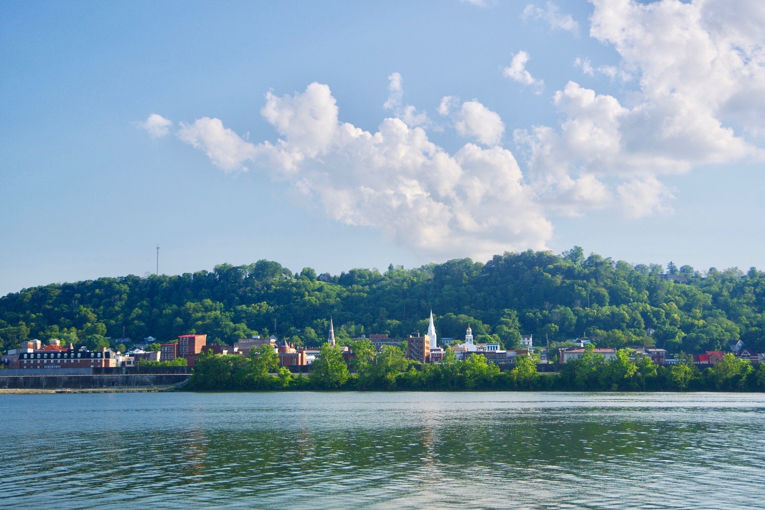 Maysville waterfront and green hills viewed across the Ohio River beneath a bright blue sky